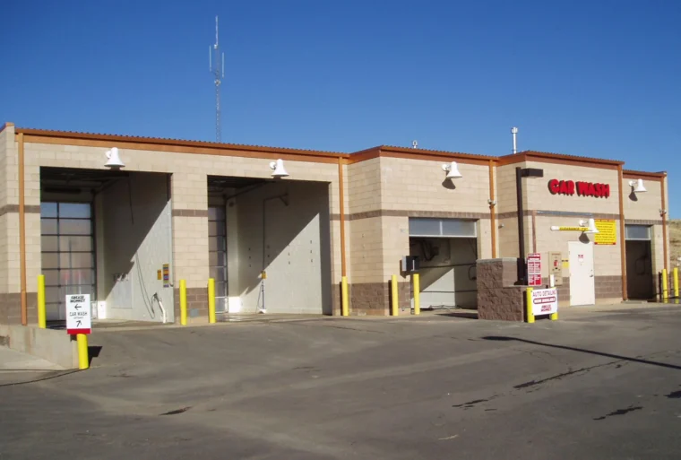 A self-service car wash facility with several wash bays, yellow poles, and instructional signs, set under a clear blue sky.
