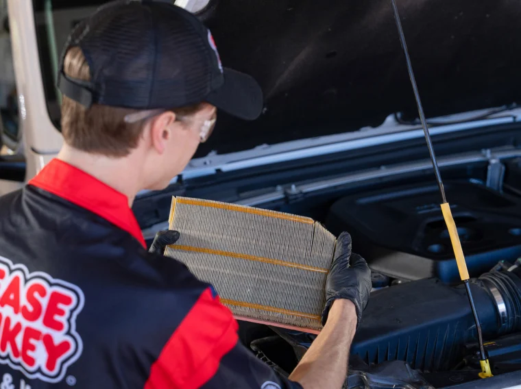 A mechanic wearing gloves and a cap inspects a rectangular air filter in front of an open car hood, demonstrating the importance of professional Filter Services for optimal vehicle performance.