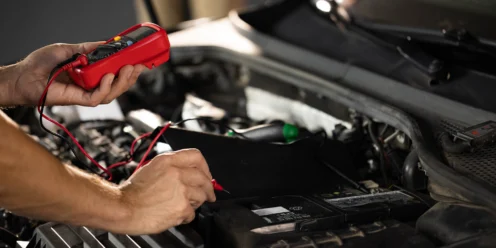 Man using multimeter to measure the voltage of a car battery.