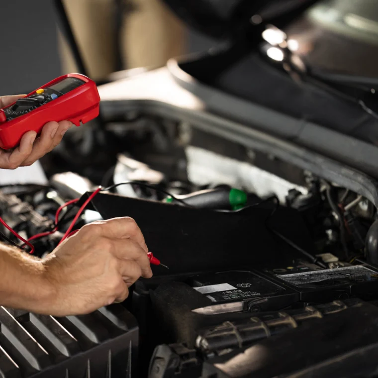 Man using multimeter to measure the voltage of a car battery.