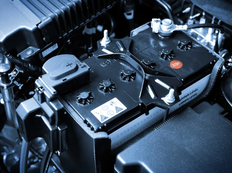 Close-up view of a car battery installed in a vehicle engine bay, showing cables, terminals, and warning labels—a clear illustration of the essential components addressed during professional Battery Services.