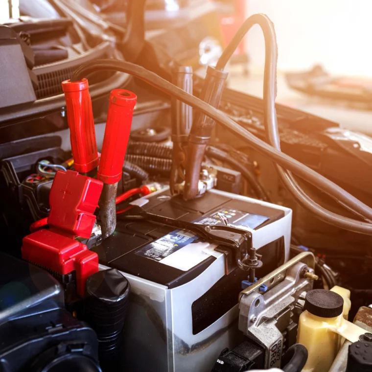 Close-up of a car battery with red and black jumper cables attached, illustrating starting services as the battery is being jump-started.
