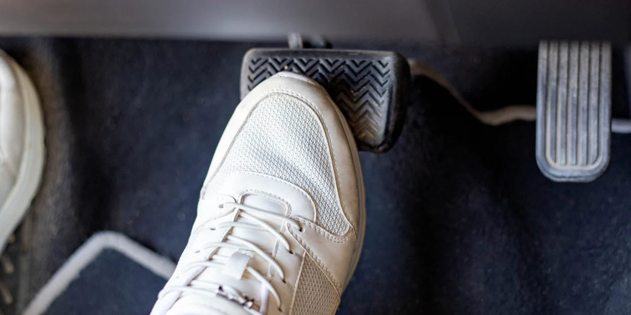 Pair of white sneakers on the floor in a car pressing the brake pedal.