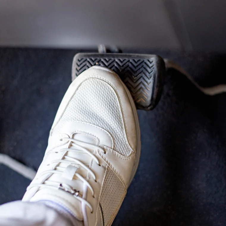 Pair of white sneakers on the floor in a car pressing the brake pedal.