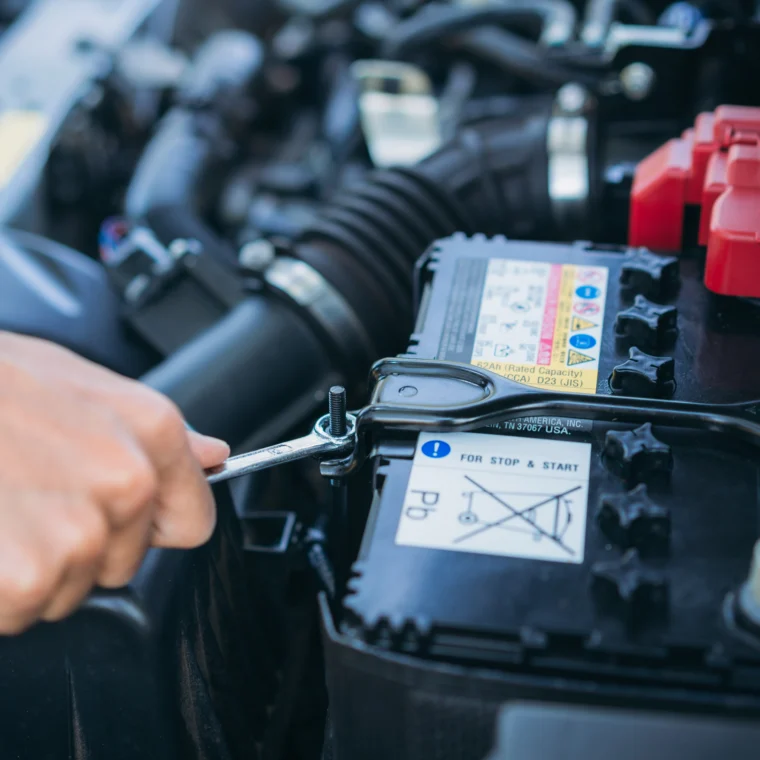An auto technicians hand is tightening a bolt that is holding a car battery.