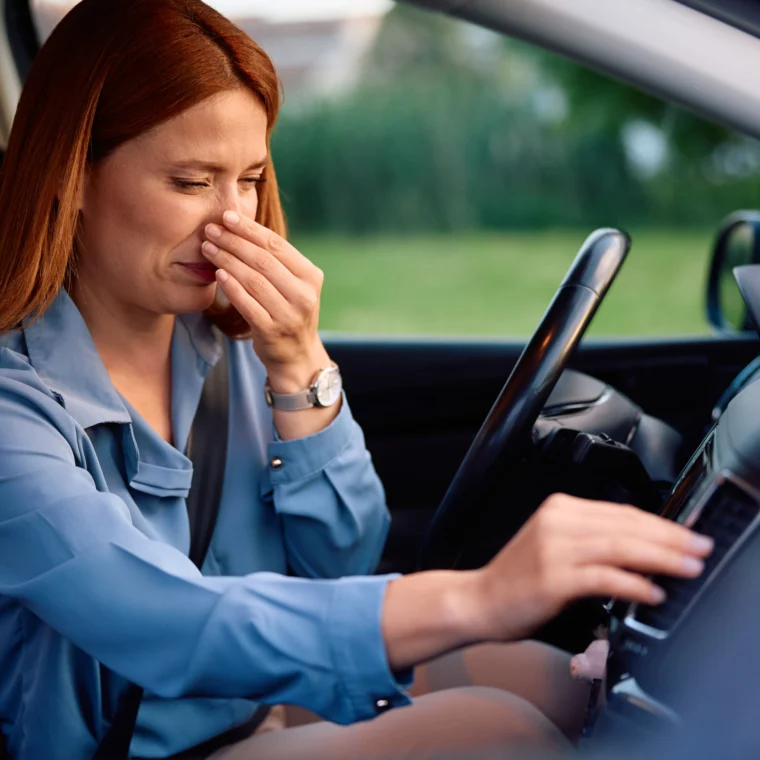 Adult woman holding her nose while turning on air conditioning in car.