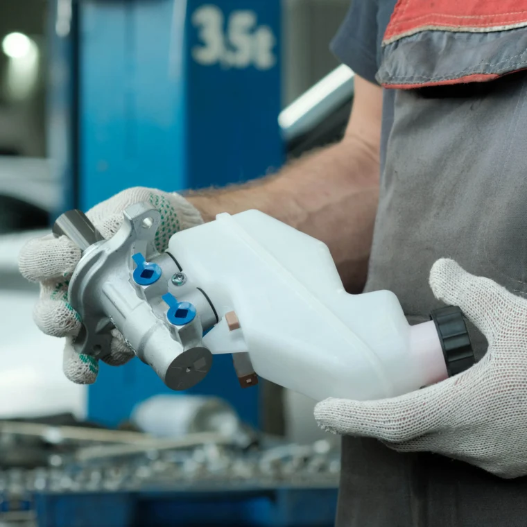 A gloved auto technician's hands holding a reservoir auto part.