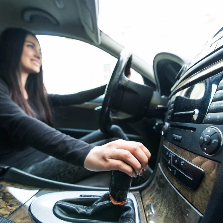 Woman sitting in the driver's seat of a vehicle and shifting the gear stick.