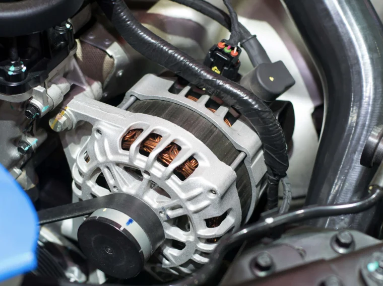 A close-up view of an automotive alternator installed in a vehicle engine bay, showing wiring and a serpentine belt—essential for reliable charging services.
