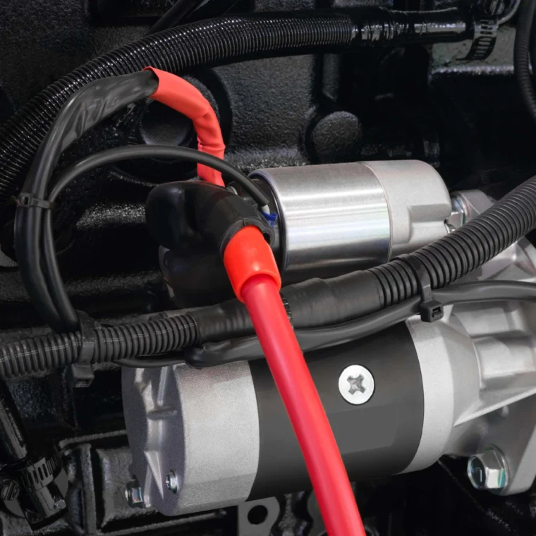 Close-up view of a car starter motor with attached red and black electrical cables and surrounding wiring, essential components for reliable starting services.