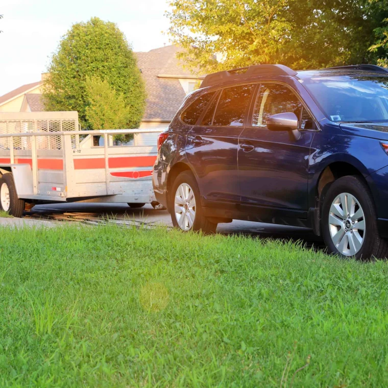 An SUV with a trailer parked outside on a street next to grass.
