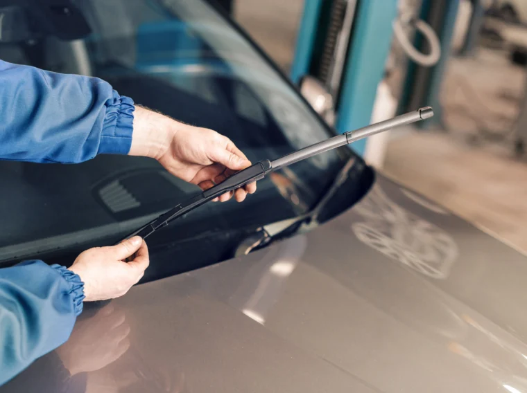 An auto technician changing windshield wipers on a car.