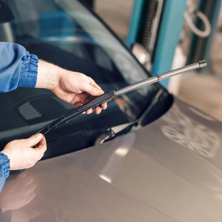 An auto technician changing windshield wipers on a car.