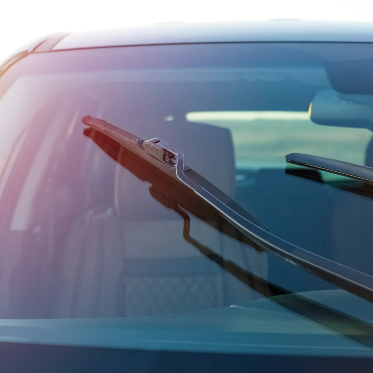 Close-up view of a car windshield with two wipers, showing the interior in the background—perfect for illustrating wiper replacement or wiper blade replacement services.