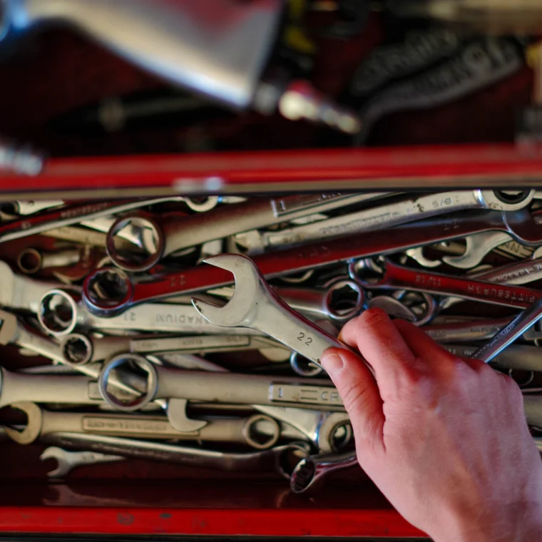 A hand picks up a wrench from a red toolbox drawer filled with various wrenches and hand tools, ready for tasks like clutch replacement.
