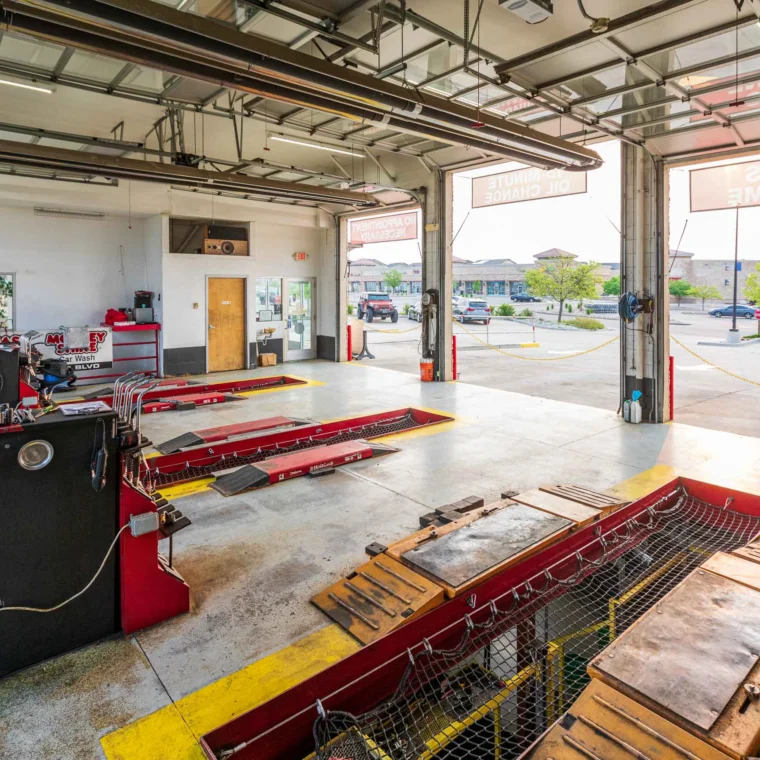 Interior of an empty auto service garage with three car bays, workstations, and large open doors—ideal for services like clutch replacement—facing a spacious parking lot.