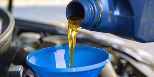 Motor oil being poured from a blue container into a blue funnel placed in a car engine compartment.