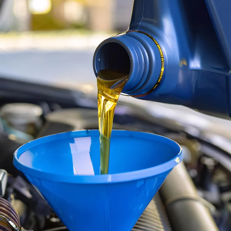 Motor oil being poured from a blue container into a blue funnel placed in a car engine compartment.