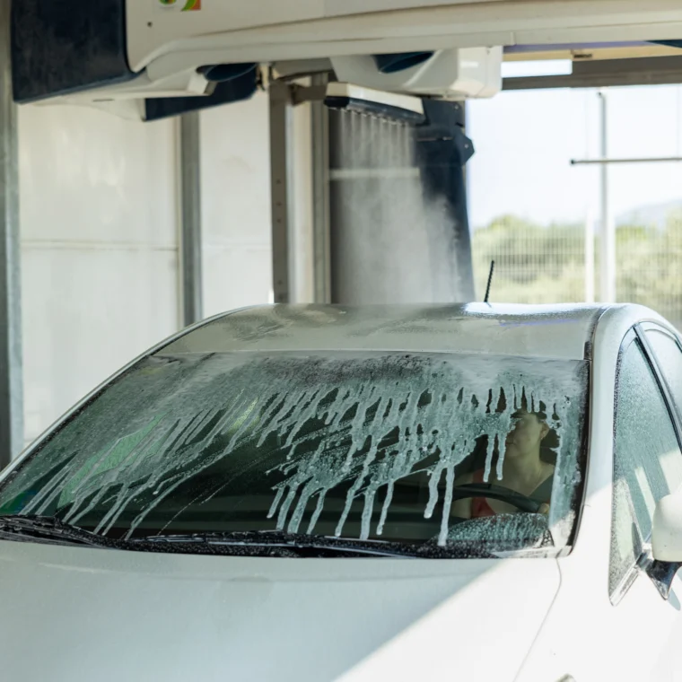 A car getting washed with a woman inside of the vehicle.