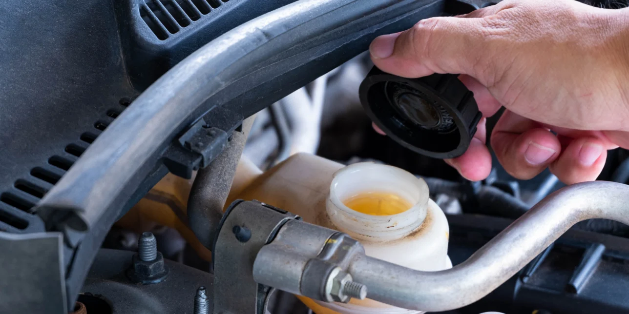 A hand holding the cap of a vehicle's brake fluid reservoir.