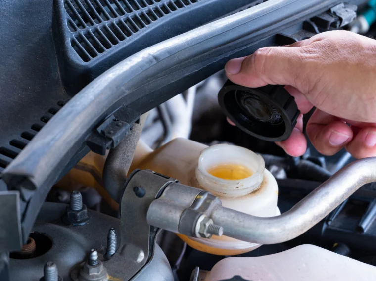 A hand holding the cap of a vehicle's brake fluid reservoir.