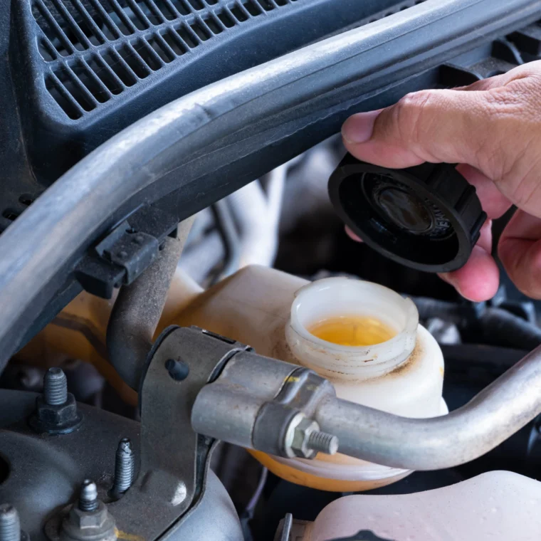 A hand holding the cap of a vehicle's brake fluid reservoir.