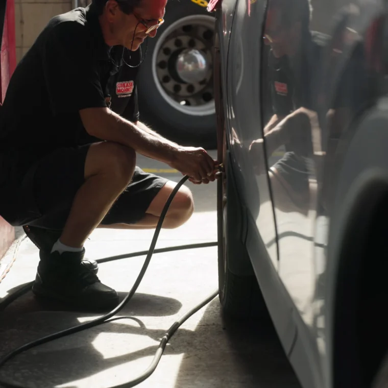 A Grease Monkey technician filling a tire with air.