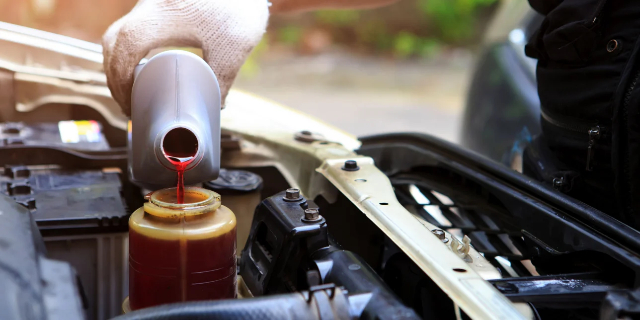 A hand filling a car's power steering fluid reservoir.