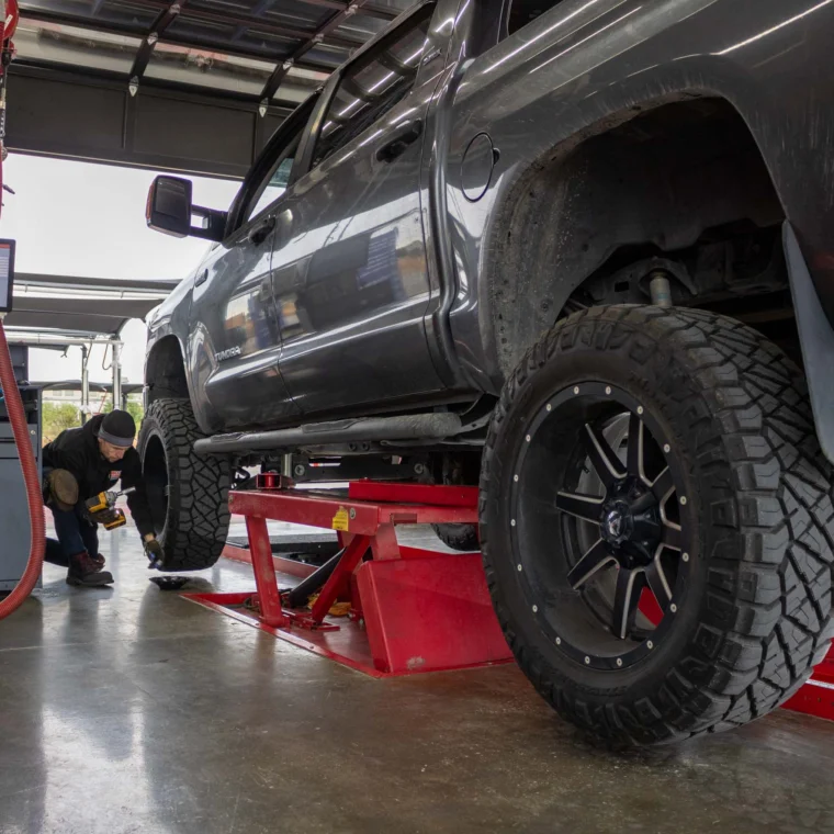 An auto technician rotating the tires of a pickup truck.
