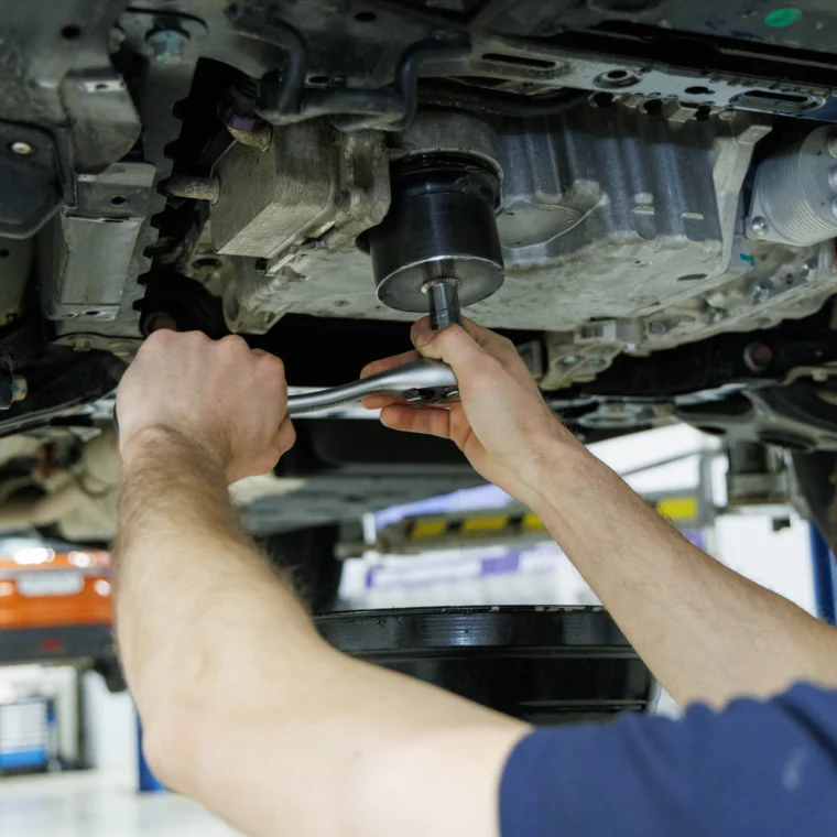 A mechanic underneath a vehicle replacing a filter.