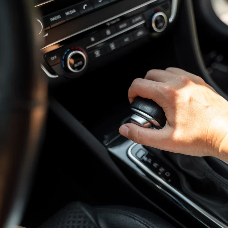 Driver hand rests on gear shift of automatic transmission in car