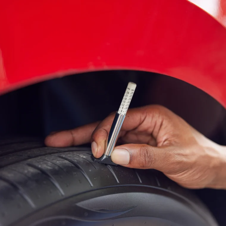 Close-up of an auto technician checking the tread of a tire with a gauge.