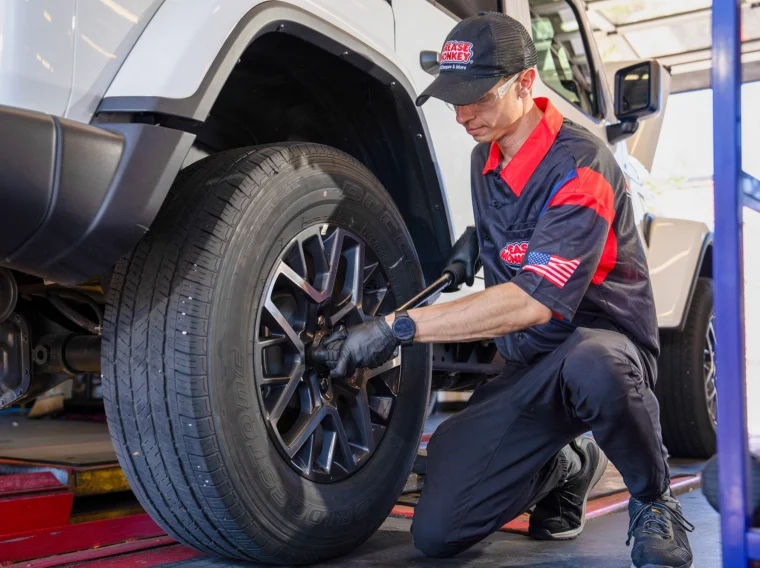 Mechanic in uniform uses a tool to tighten lug nuts on the front wheel of a white SUV inside an auto repair shop, demonstrating expert Tire Services.