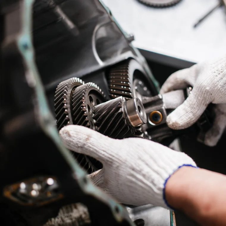 A person wearing white work gloves adjusts gears inside a mechanical assembly—likely part of an engine or transmission services setup.