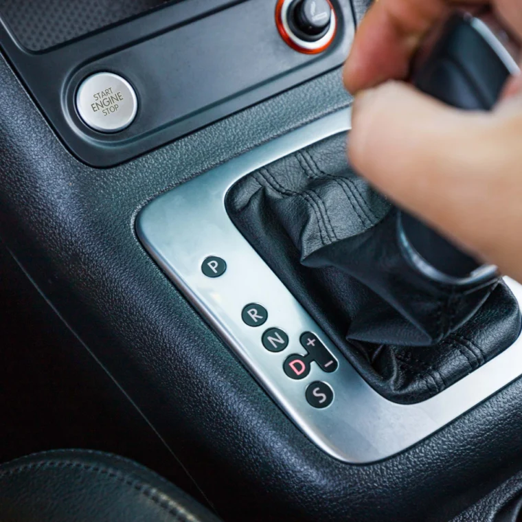 A hand shifting the gear lever of an automatic transmission, with gear positions P, R, N, D, and manual (+/-) modes visible—highlighting the importance of regular Transmission Services for smooth operation.