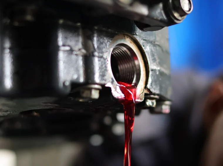 Red transmission fluid drains from the open port of a vehicle’s transmission system during a Fluid Exchange Services maintenance procedure.