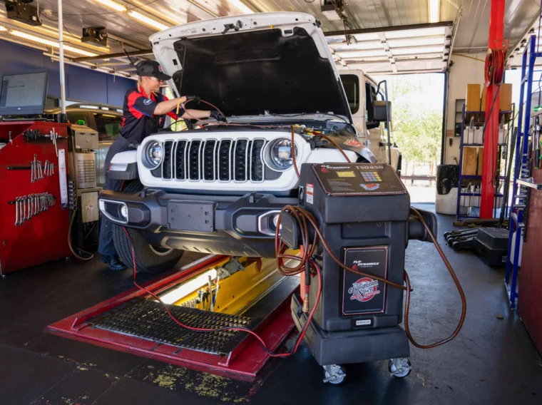 A mechanic inspects a Jeep SUV with its hood open inside an auto repair shop. Diagnostic equipment is connected to the vehicle as part of routine maintenance, including Fluid Exchange Services.