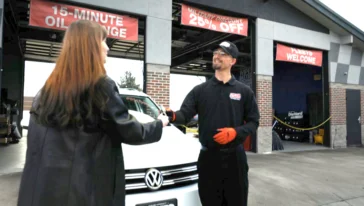 A Grease Monkey mechanic standing in front of three bay doors handing a woman a set of keys.