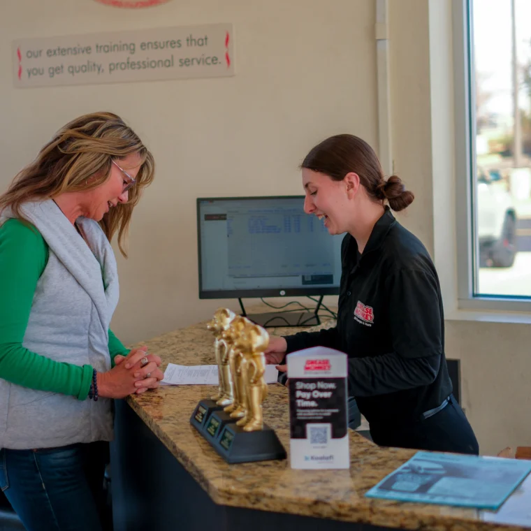 A customer and an employee interact at a Grease Monkey service counter, with trophies and informational materials highlighting their Engine Services displayed on the countertop.