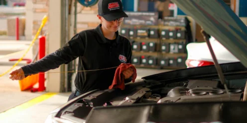 A mechanic in a Grease Monkey uniform checks the oil level under the hood of a vehicle, showcasing expert Engine Services inside an auto service garage.