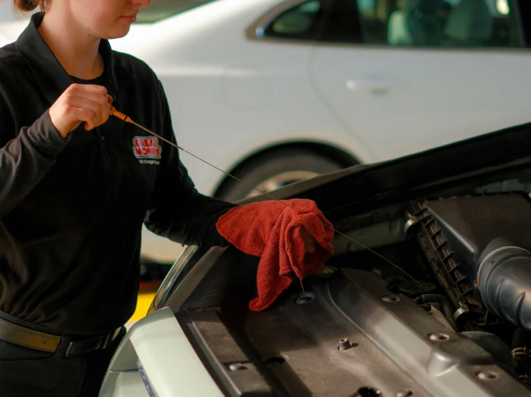 An auto mechanic in uniform checks the oil level of a car engine with a dipstick while holding a red cloth, ensuring top-notch Fluid Exchange Services.