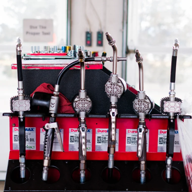 A row of oil dispensing nozzles mounted above oil containers and tools in a garage, ready for efficient Fluid Exchange Services in a service station setting.