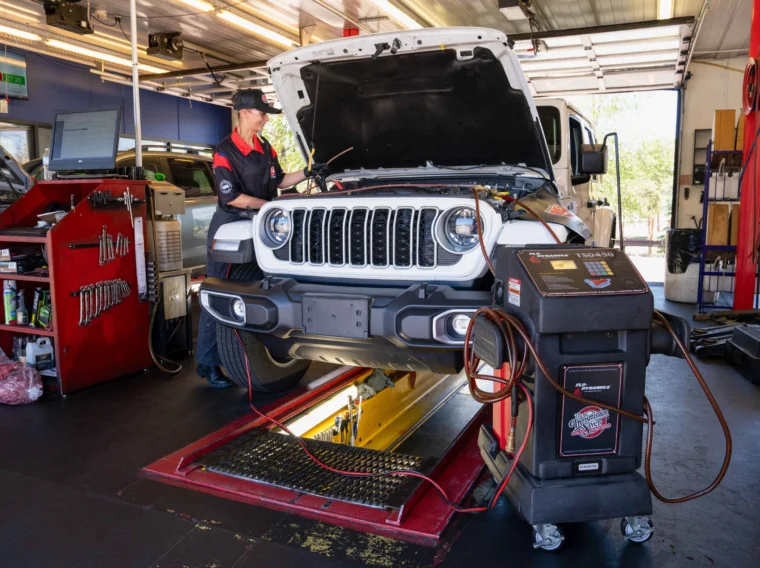 A mechanic conducts maintenance on a white SUV with its hood open inside an auto repair shop, using diagnostic equipment connected to the vehicle while preparing to perform Fluid Exchange Services.