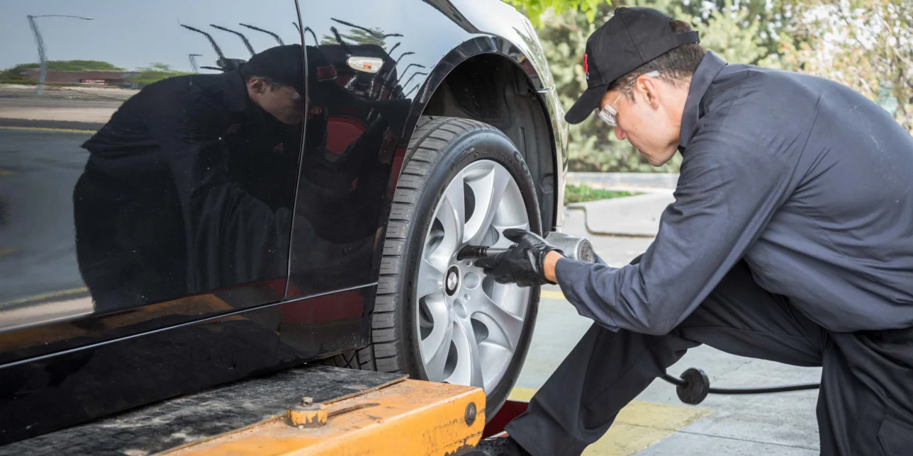A mechanic in uniform uses a power tool to tighten the lug nuts on a car wheel at an auto shop, ensuring vehicles are ready for State Inspection Services.