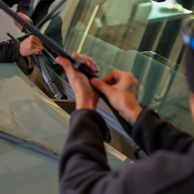 Two people are installing or replacing windshield wiper blades on a car as part of routine maintenance and State Inspection Services.