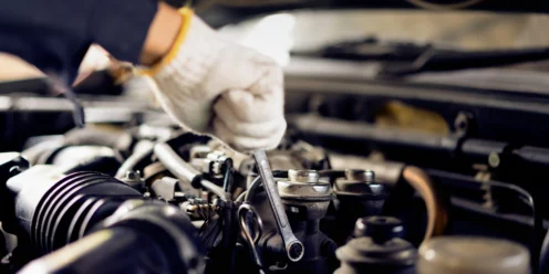 A person wearing a white glove uses a wrench to work on a car engine, highlighting the importance of preventive maintenance, with various engine components visible.