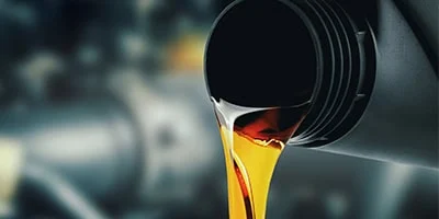 Close-up of golden-brown high mileage oil being poured from a plastic container, highlighting oil differences against a blurred background.