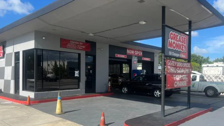 A Grease Monkey oil change shop with an overhang, signage, and cars parked in service bays on a sunny day. Orange traffic cones are near the entrance.