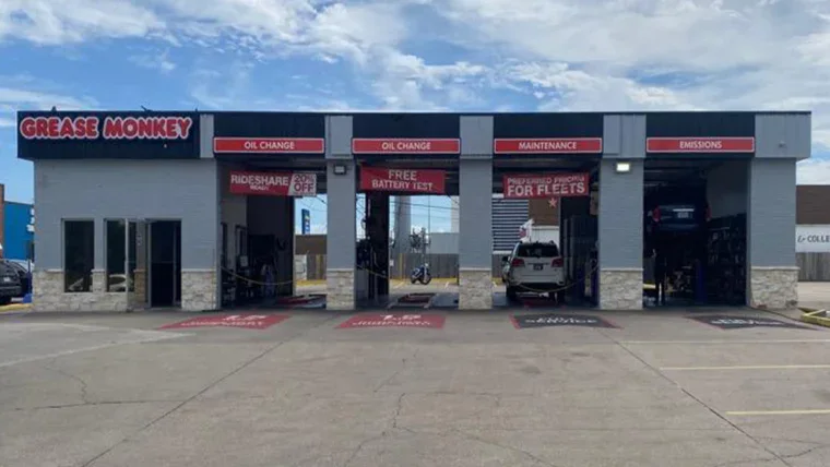 A Grease Monkey auto service center with three open service bays labeled oil change, maintenance, and emissions; one car is being serviced inside.
