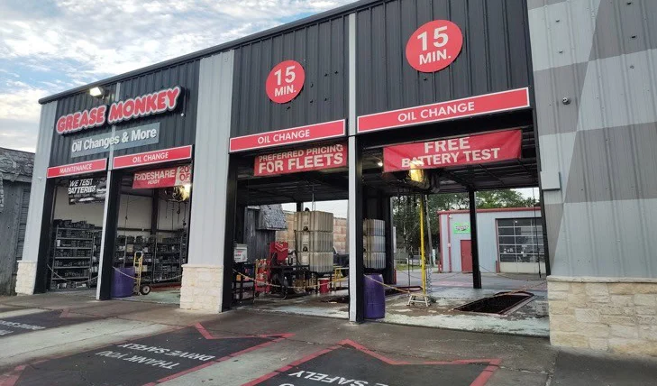 Exterior of a Grease Monkey auto service shop with open garage bays offering 15-minute oil changes, preferred fleet pricing, and free battery tests.